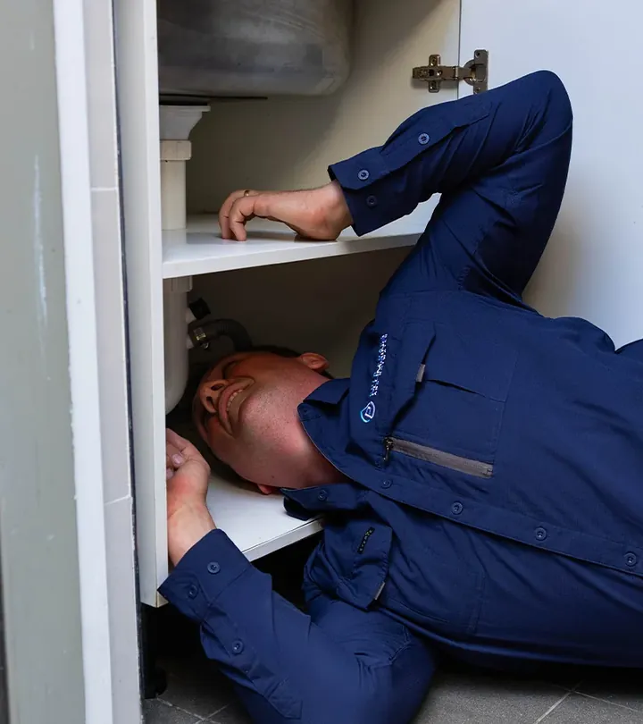 Emergency plumber repairing pipework under a laundry sink